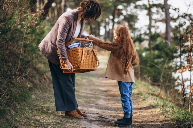 Mujer joven con hija en bosque con caja de picnic