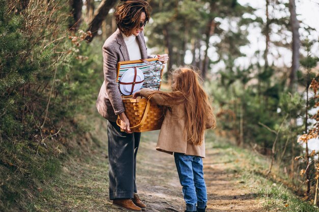 Mujer joven con hija en bosque con caja de picnic