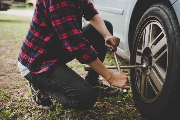 Mujer joven hipster comprobación de un neumático plano en su coche tratar de arreglar.