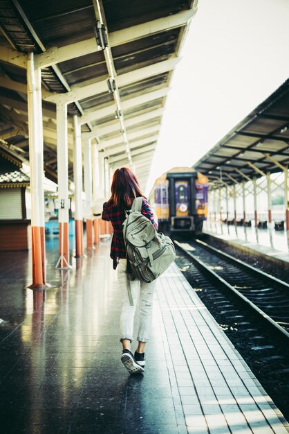 Mujer joven hipster esperando en la plataforma de la estación con la mochila. Concepto de viaje.