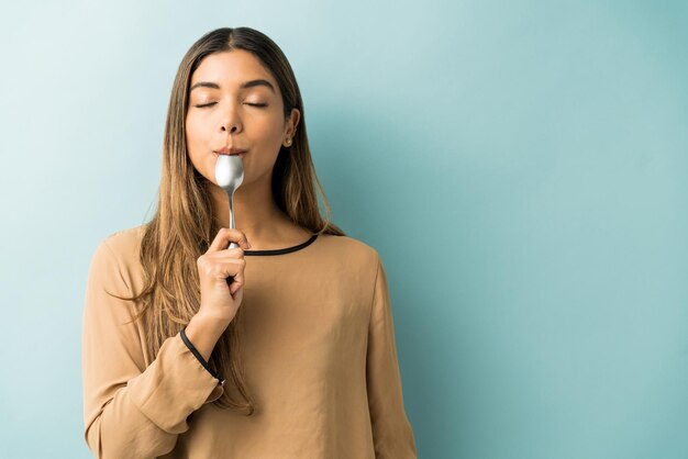 Mujer joven hispana cuchara de degustación mientras está de pie sobre fondo azul.