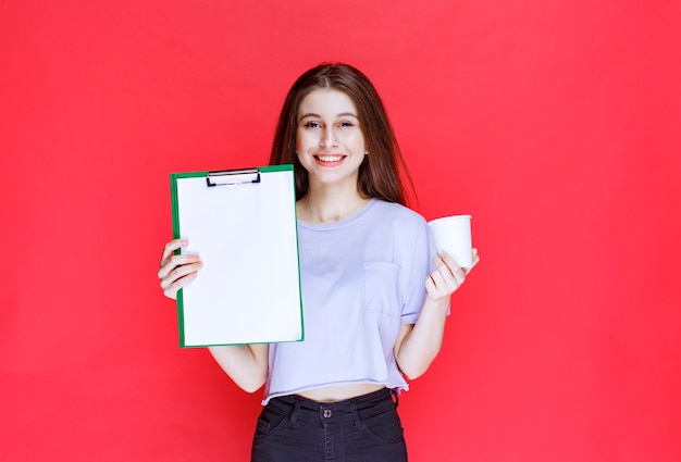 mujer joven con hoja de informe y una taza de bebida.