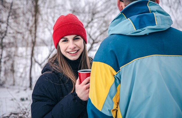 Una mujer joven con un hombre en un paseo en invierno con una taza termo