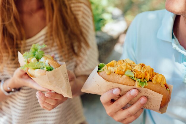 Mujer joven y hombre con perro caliente en las manos, comer comida callejera