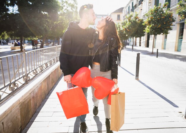 Mujer joven y hombre sonriente con paquetes y globos divirtiéndose en la calle