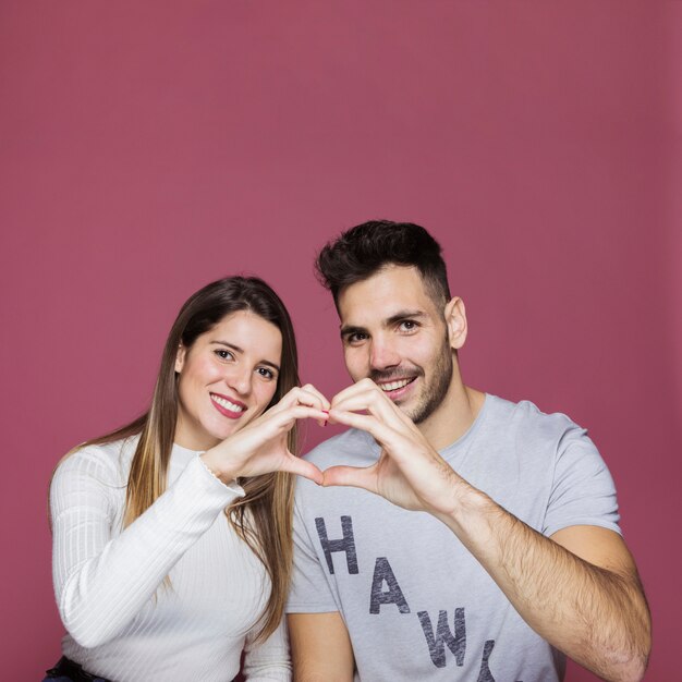 Mujer joven y hombre sonrientes que muestran el corazón por las manos