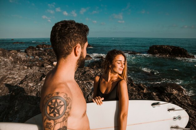 Mujer joven y hombre con tablas de surf en la costa de roca cerca del mar