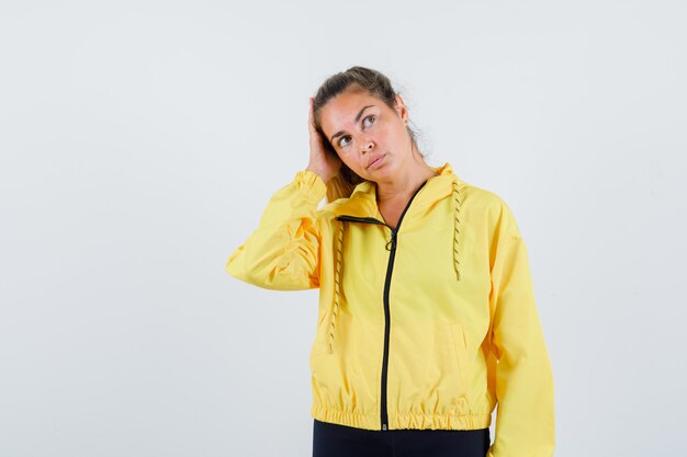 Mujer joven en impermeable amarillo ajustando su cabello mientras mira a un lado y mira enfocado