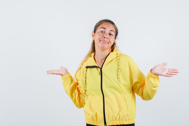 Mujer joven en impermeable amarillo mostrando gesto idk y mirando vanidoso
