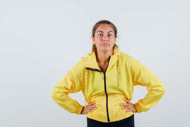 Mujer joven en impermeable amarillo tomados de la mano en la cintura y mirando enfocado