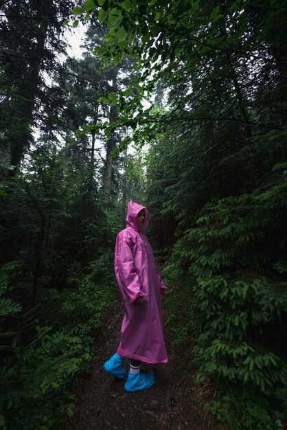 Mujer joven en un impermeable camina por el bosque bajo la lluvia