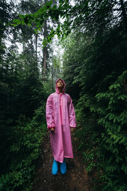 Mujer joven en un impermeable camina por el bosque bajo la lluvia