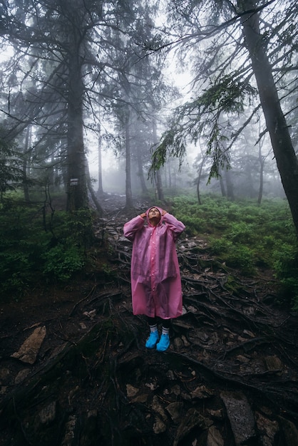 Mujer joven en un impermeable camina por el bosque bajo la lluvia