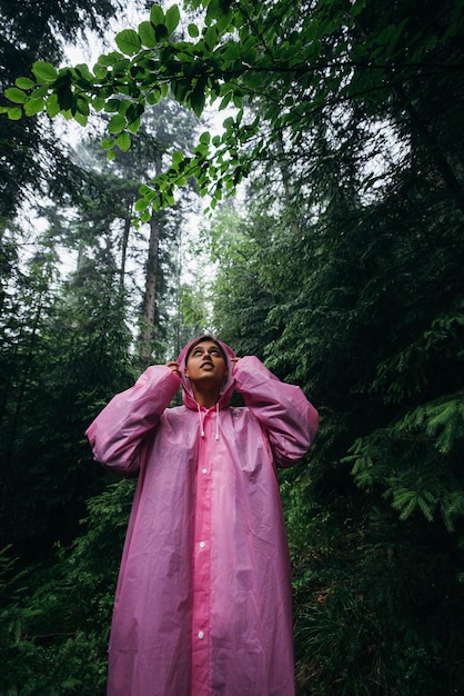 Mujer joven en un impermeable camina por el bosque bajo la lluvia