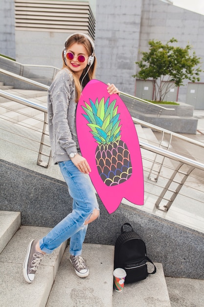 Mujer joven inconformista en la calle con tabla de equilibrio vistiendo suéter y jeans