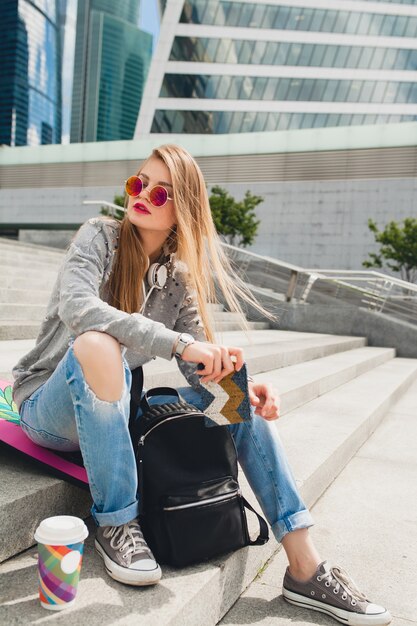 Mujer joven inconformista en la calle con tabla de equilibrio vistiendo suéter y jeans