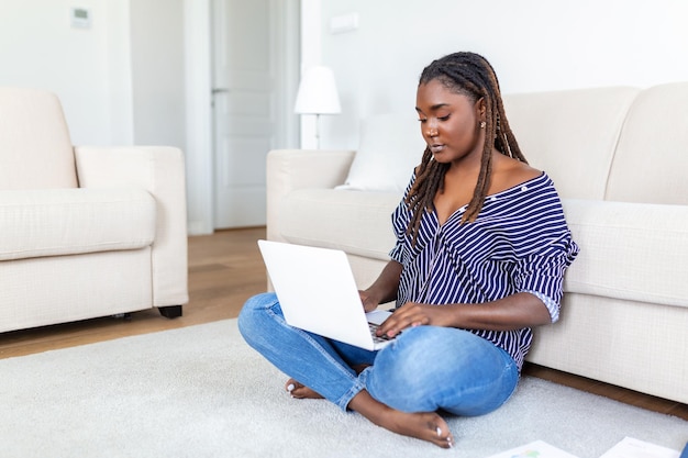 Mujer joven independiente positiva viendo video en el blog en el netbook y tomando un café en una casa cómoda Mujer joven de negocios hermosa trabajando en una computadora portátil Freelancer conectándose a Internet
