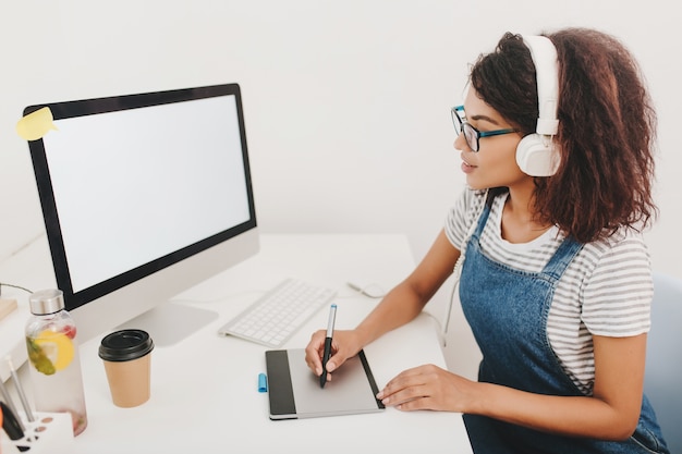 Mujer joven inspirada en camisa a rayas mirando la pantalla del ordenador y trabajando con tableta