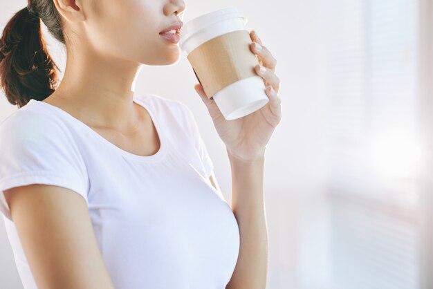 Mujer joven irreconocible bebiendo café para llevar en la mañana