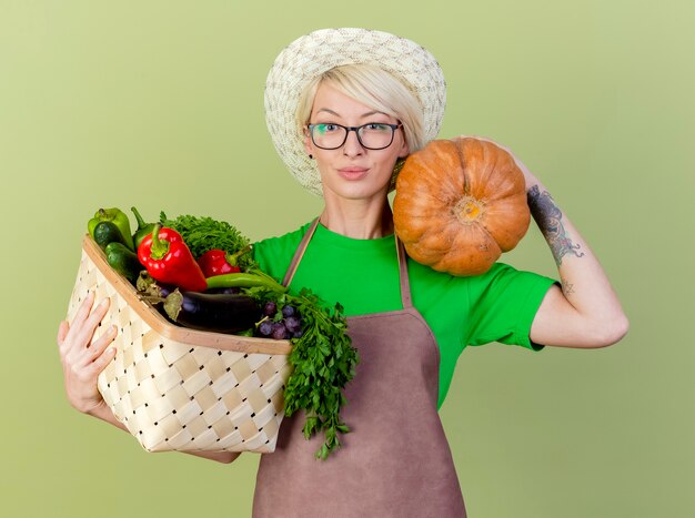 Mujer joven jardinero con pelo corto en delantal y sombrero con calabaza