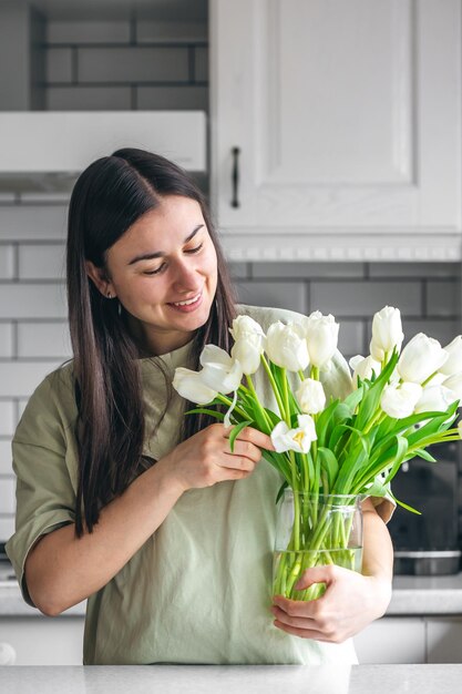 Mujer joven y jarrón con un ramo de tulipanes blancos en la cocina