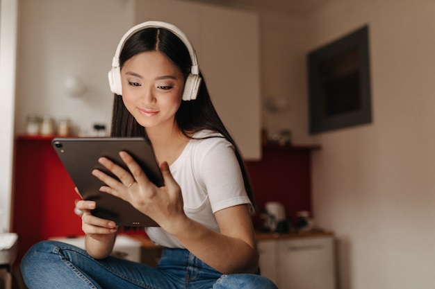 Mujer joven en jeans y camiseta blanca mira tableta y escucha música en auriculares