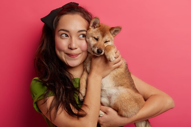 Mujer joven juega con una encantadora mascota doméstica, enfocada arriba con expresión alegre, consuela al perro shiba inu, posa con un animal devoto