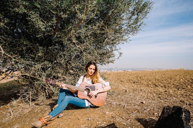 Mujer joven, juego, guitarra, cerca, arbusto