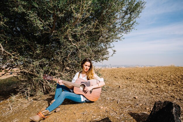 Mujer joven, juego, guitarra, cerca, arbusto