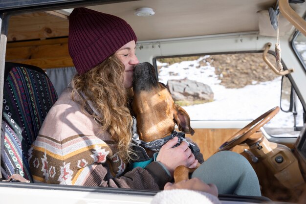 Mujer joven jugando con su perro dentro de la autocaravana durante el viaje de invierno