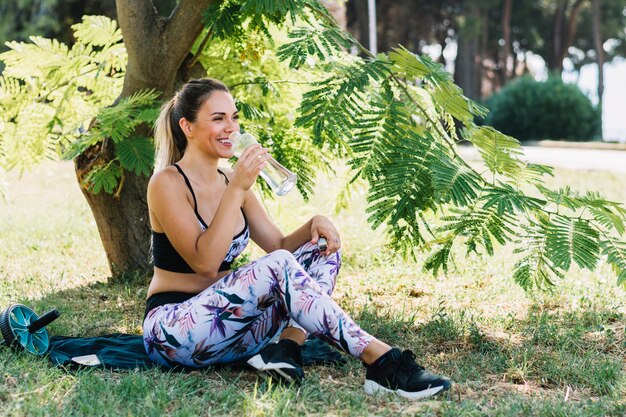 Mujer joven juguetona que goza del agua potable de la botella en el jardín