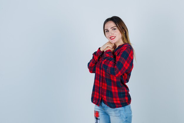 Mujer joven juntando las manos en gesto de oración en camisa a cuadros y mirando alegre. vista frontal.