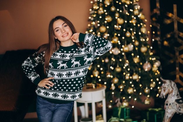 Mujer joven junto al árbol de Navidad con luces brillantes de Navidad