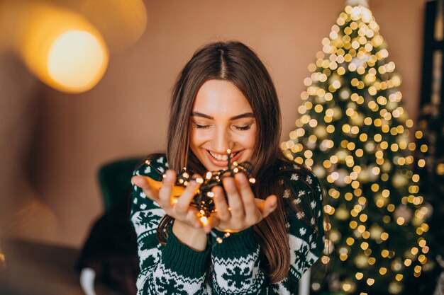 Mujer joven junto al árbol de Navidad con luces brillantes de Navidad