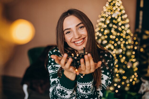 Mujer joven junto al árbol de Navidad con luces brillantes de Navidad