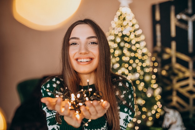 Mujer joven junto al árbol de Navidad con luces brillantes de Navidad