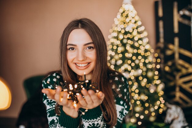 Mujer joven junto al árbol de Navidad con luces brillantes de Navidad