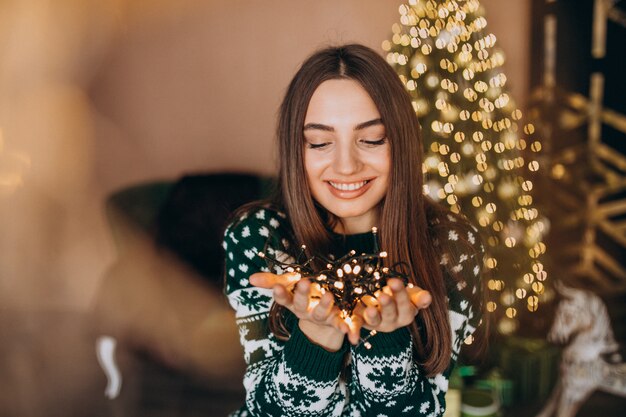 Mujer joven junto al árbol de Navidad con luces brillantes de Navidad