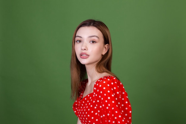 Mujer joven con labios grandes marrones de maquillaje natural perfecto en vestido rojo de lunares en pared verde posando