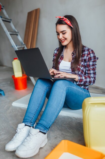 Mujer joven con laptop haciendo reparaciones en casa nueva