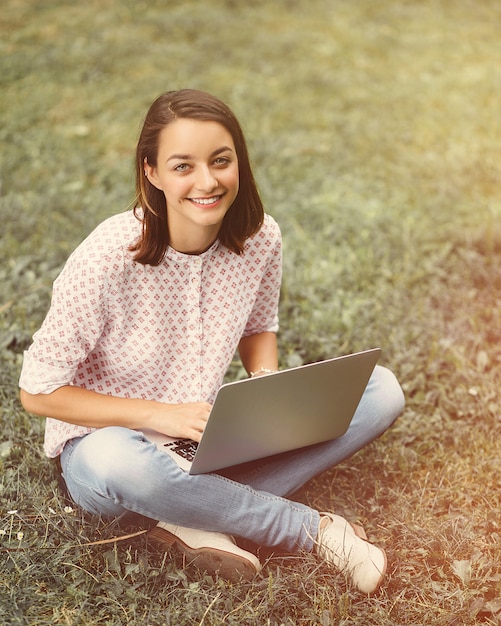 Mujer joven con laptop sentada sobre la hierba verde