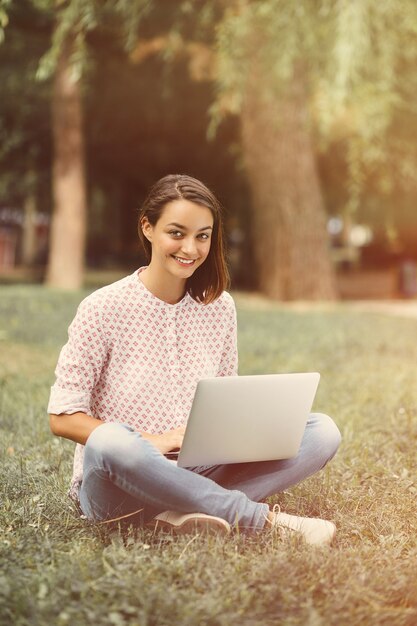 Mujer joven con laptop sentada sobre la hierba verde