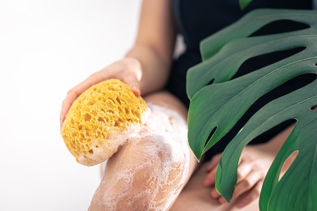 Mujer joven lavándose las piernas con esponja amarilla y espuma de jabón