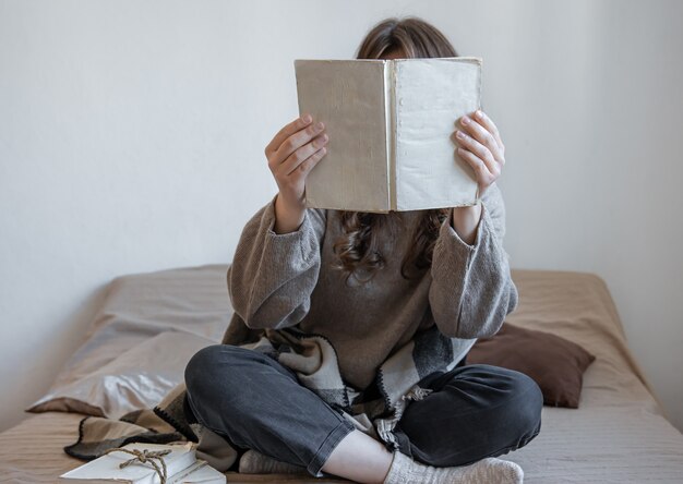 Mujer joven lee un libro mientras está sentado en la cama