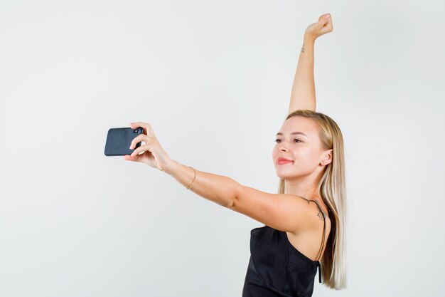 Mujer joven levantando el brazo mientras toma selfie en camiseta negra