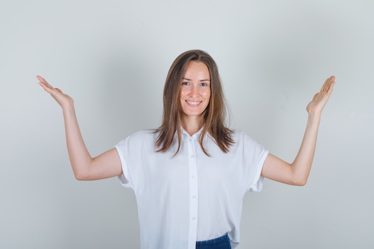 Foto gratuito mujer joven levantando los brazos en camiseta blanca, jeans y mirando alegre