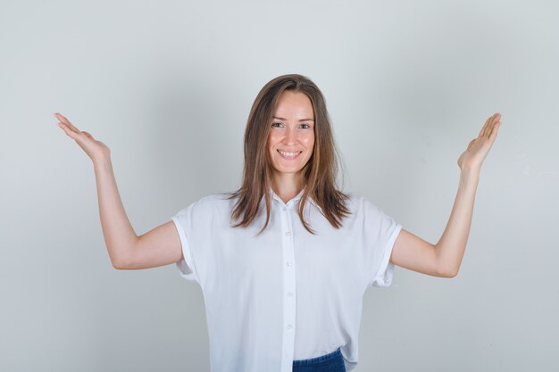 Mujer joven levantando los brazos en camiseta blanca, jeans y mirando alegre