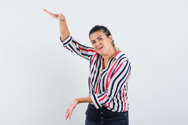 Mujer joven levantando los brazos como mostrando escamas en blusa rayada y luciendo optimista