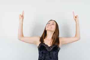 Foto gratuita mujer joven levantando los brazos con dos dedos en camiseta negra y mirando feliz