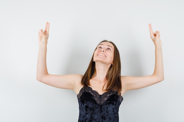 Mujer joven levantando los brazos con dos dedos en camiseta negra y mirando feliz